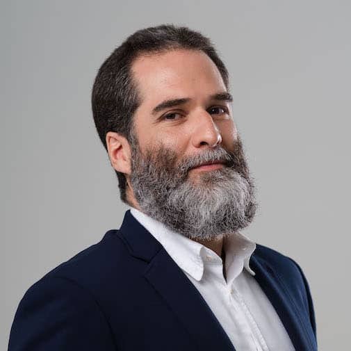 Homem com barba grisalha, vestindo blazer e camisa branca, representando médicos pelo clima e saúde ambiental.