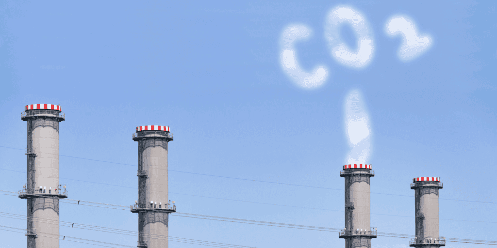 Texto alternativo: Torres de fábricas emitindo fumaça, contribuindo para a poluição atmosférica e mudanças climáticas globais.